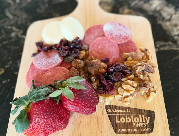 board with cheese, fruits, nuts, and salami sitting on a table